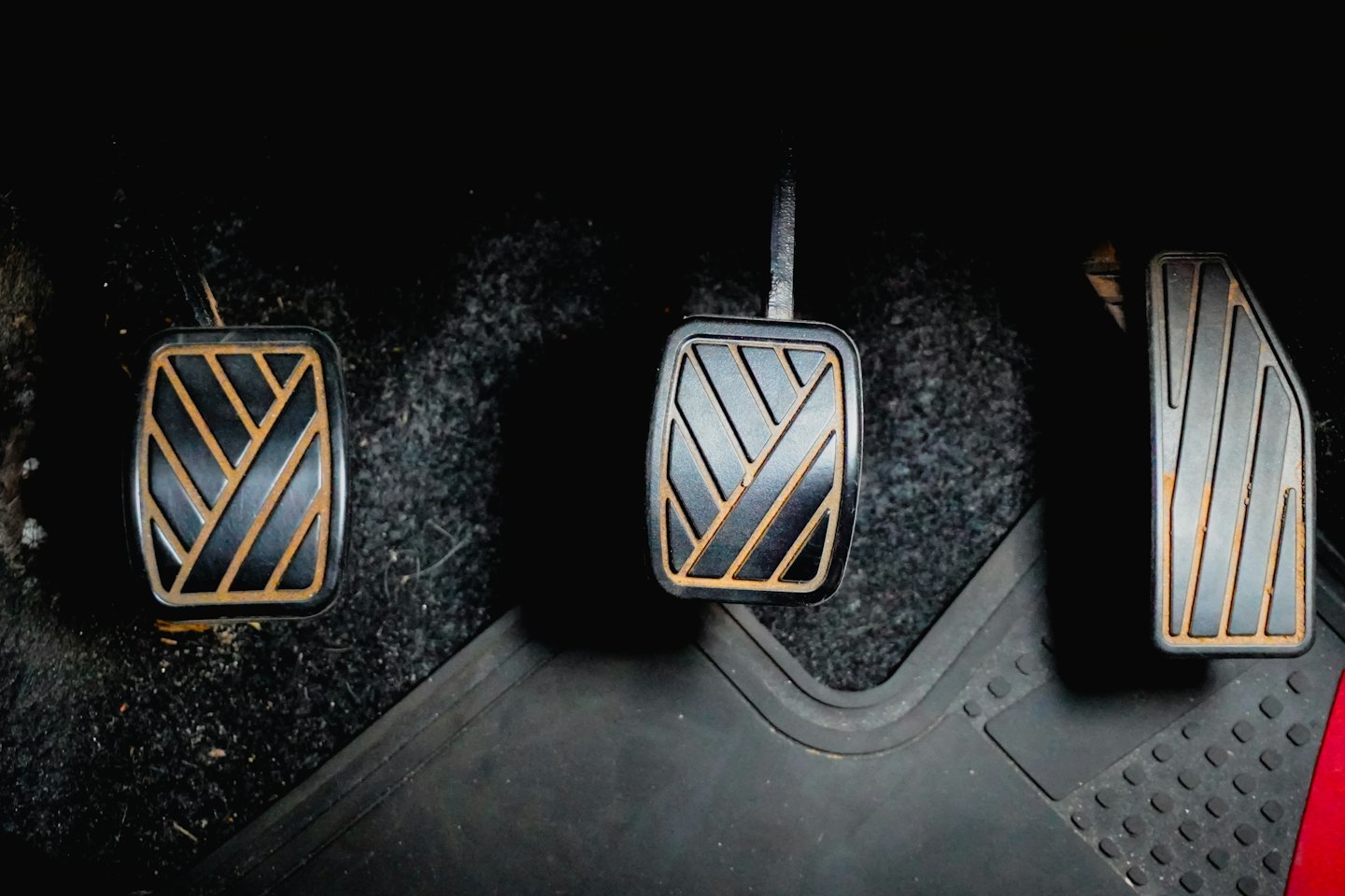 Three worn manual transmission car pedals over a rubber mat.