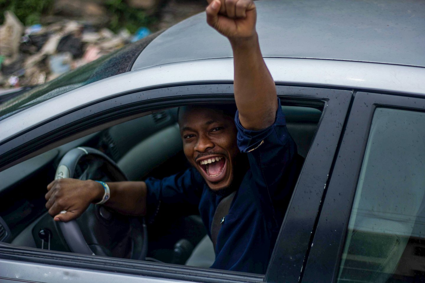 Man joyfully pumps fist out car window.