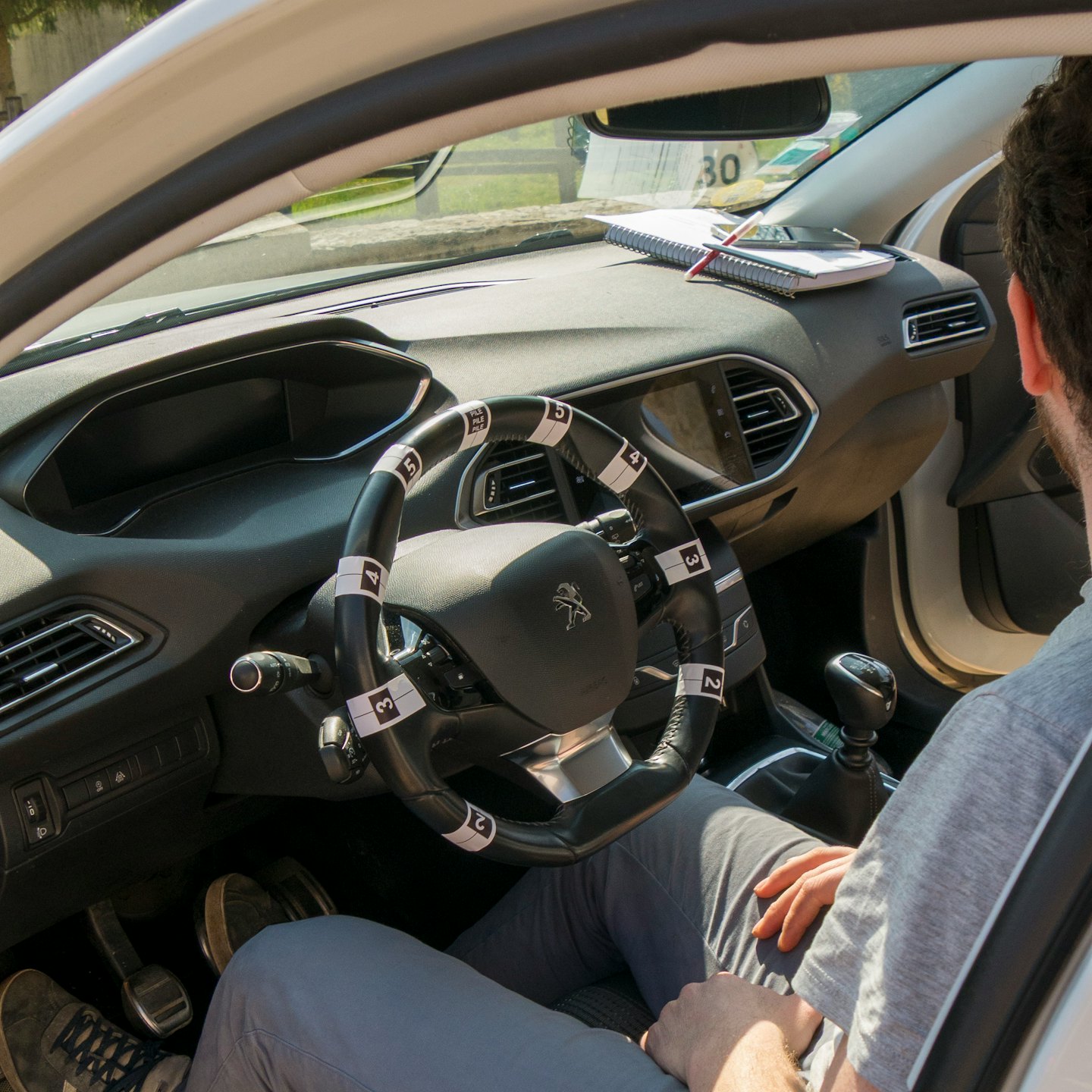 Student sits in a car with numbered steering wheel controls.